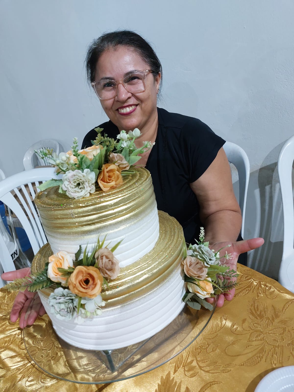 Confeiteira do buffet apresentando um bolo de dois andares em branco e dourado