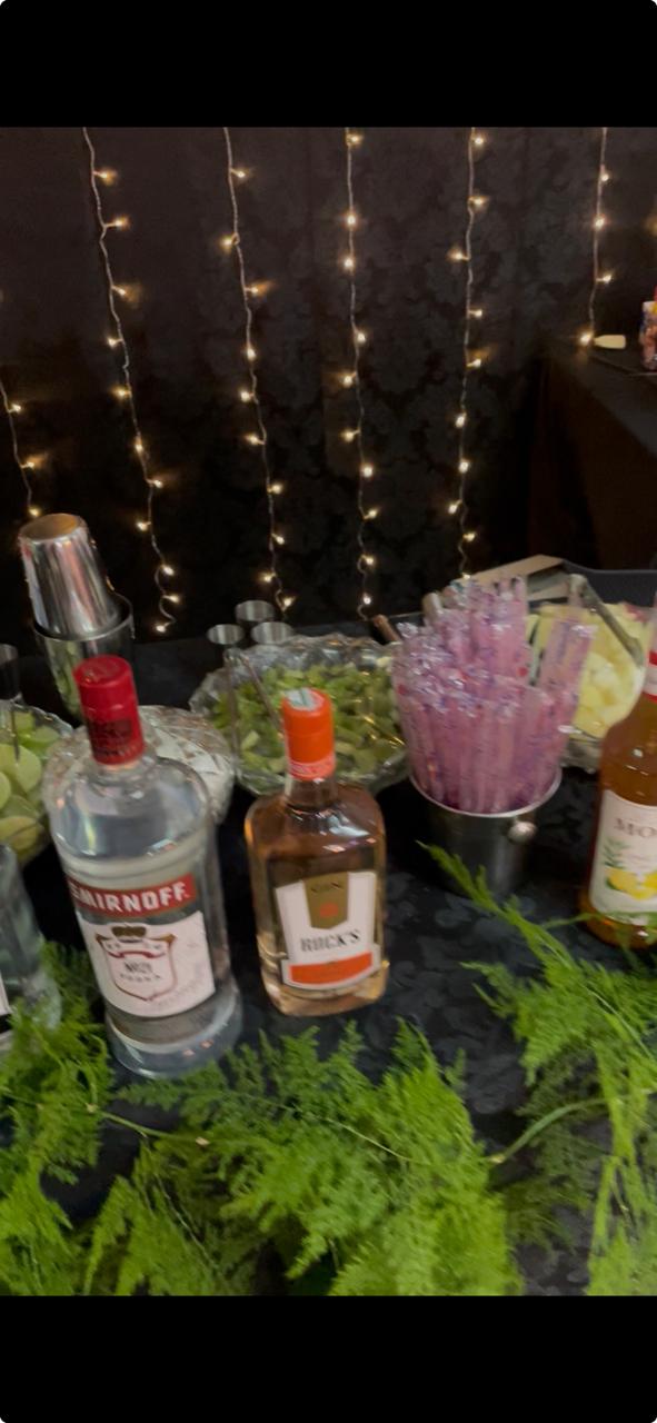 Estação de drinks com garrafas de vodka e gin, coqueteleira e tigela com limões fatiados